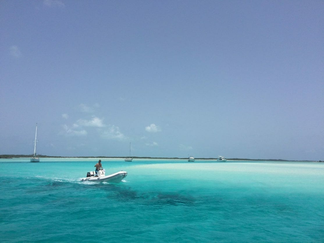 A man on a boat sailing it the crystalline turquoise water of Exuma, the Bahamas