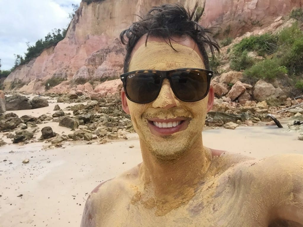 Pericles Rosa is covered with mud and some rocks behind him on Gamboa Beach, Bahia, Brazil