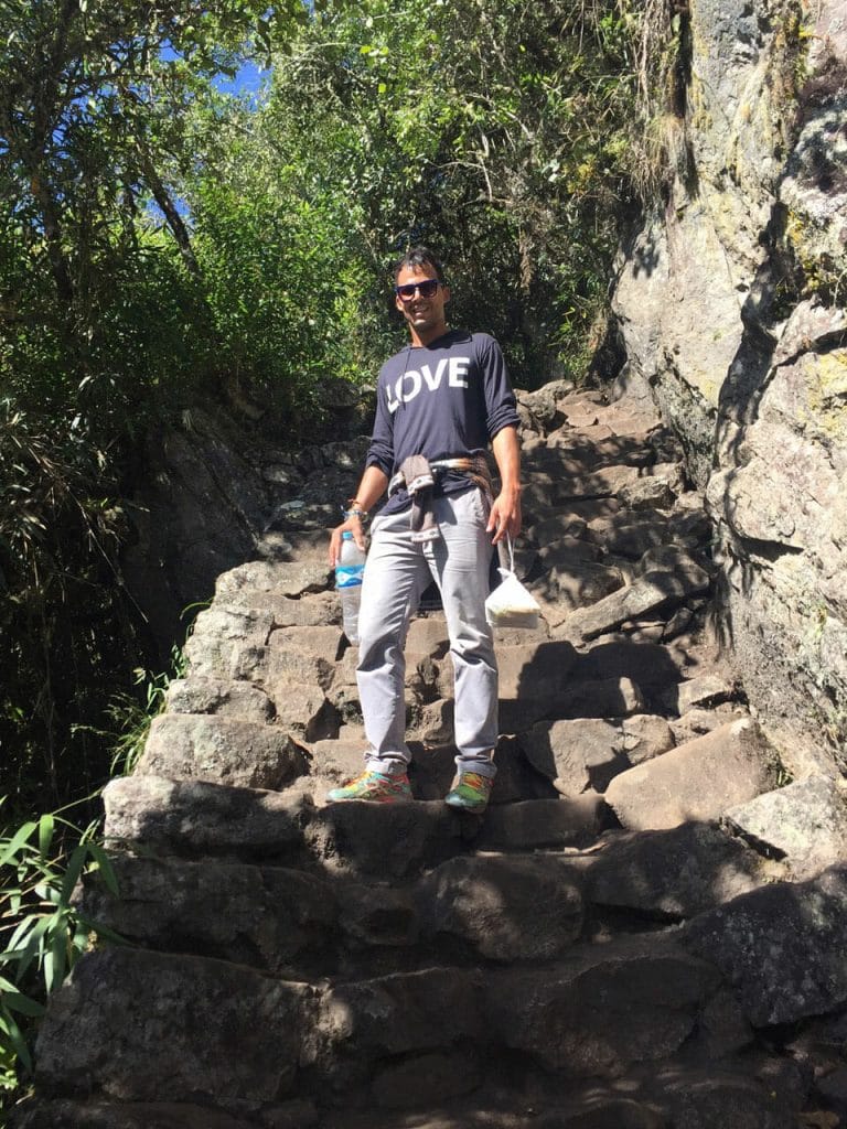 Um homem de pé com uma camiseta manga longa preta e calça jeans nos degraus da trilha da Montanha Machu Picchu