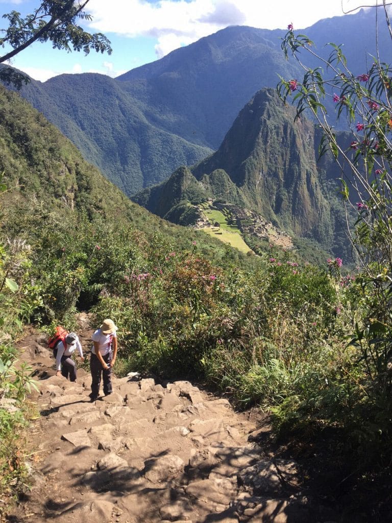 Um casal subindo os degraus degraus da trilha da Montanha Machu Picchu com várias montanhas ao fundo