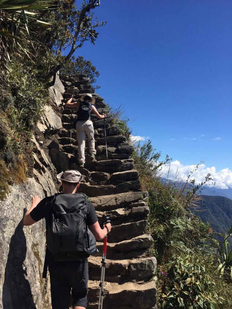 Um casal subindo uma escada super íngrime com proteção apenas no lado esquerdo na Montanha Machu Picchu, Peru