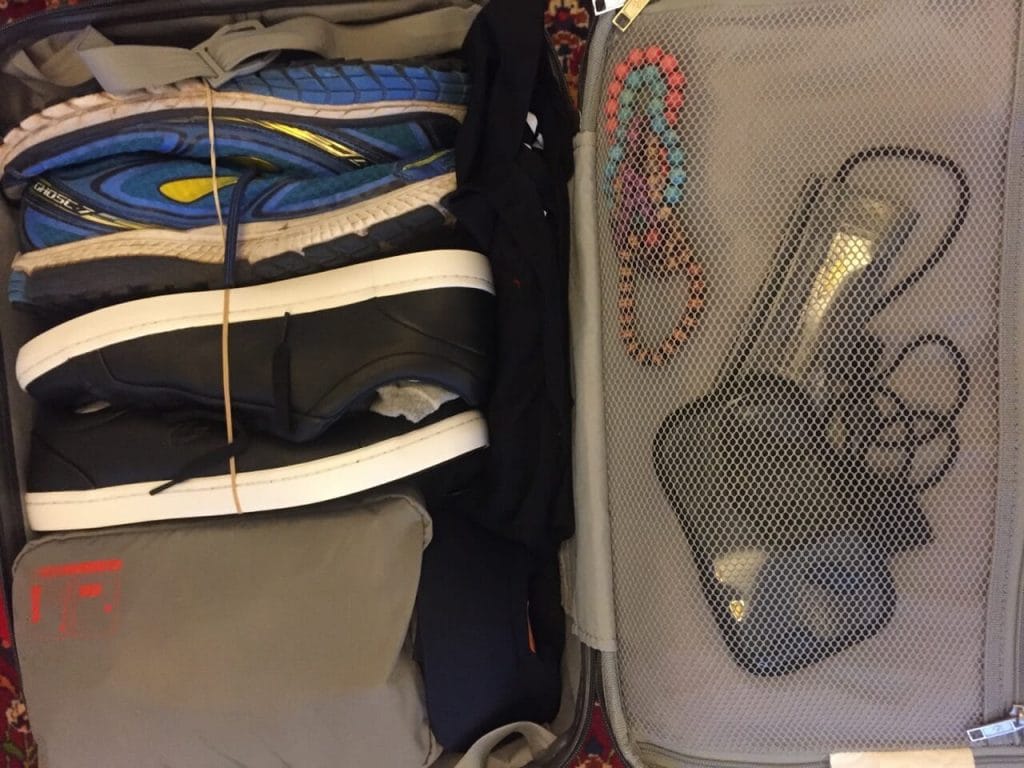 Two pairs of shoes, a toiletry bag, bracelets and phone case inside a carry-on suiticase