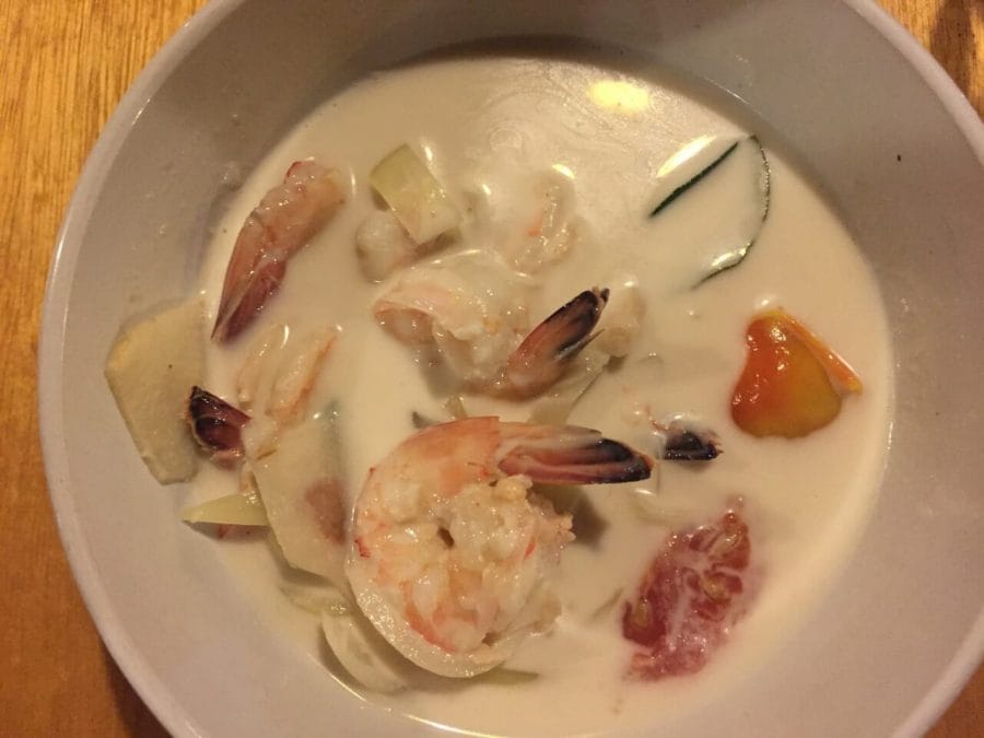 Um bowl branco com sopa de frango, camarão e leite de coco 