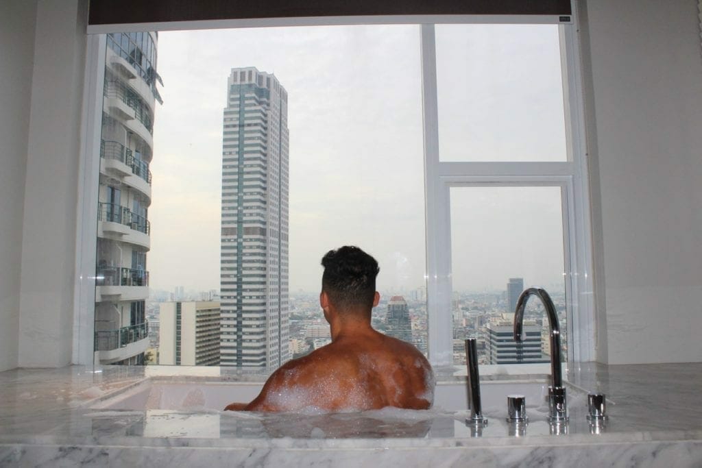 um homem na banheiro de um quarto do hotel Mode Sathorn admirando a vista do skyline de Bangkok
