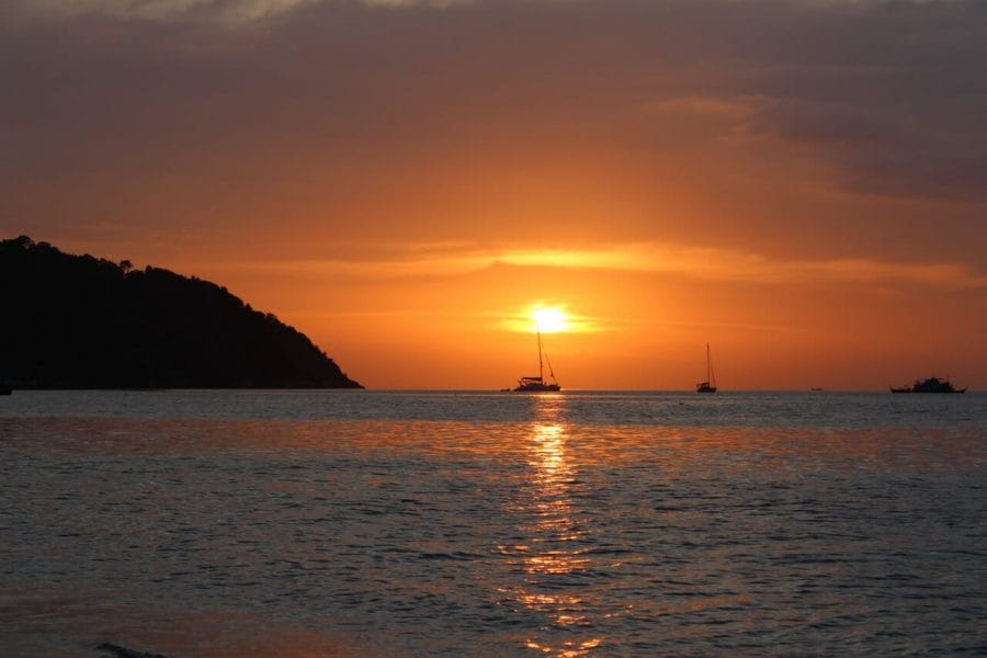 Sunset on Sunset Beach with golden-orange sky, boats on the water and a mountain covered with vegetation
