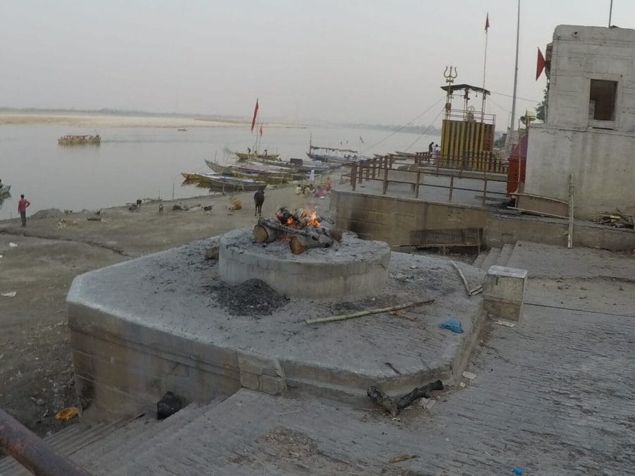 a round cemented platform with some woods burning and the Ganges River water