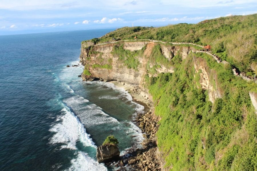 A sea cliff on the southwestern coast of Bali covered by low vegetation and a beach with crystal-clear water