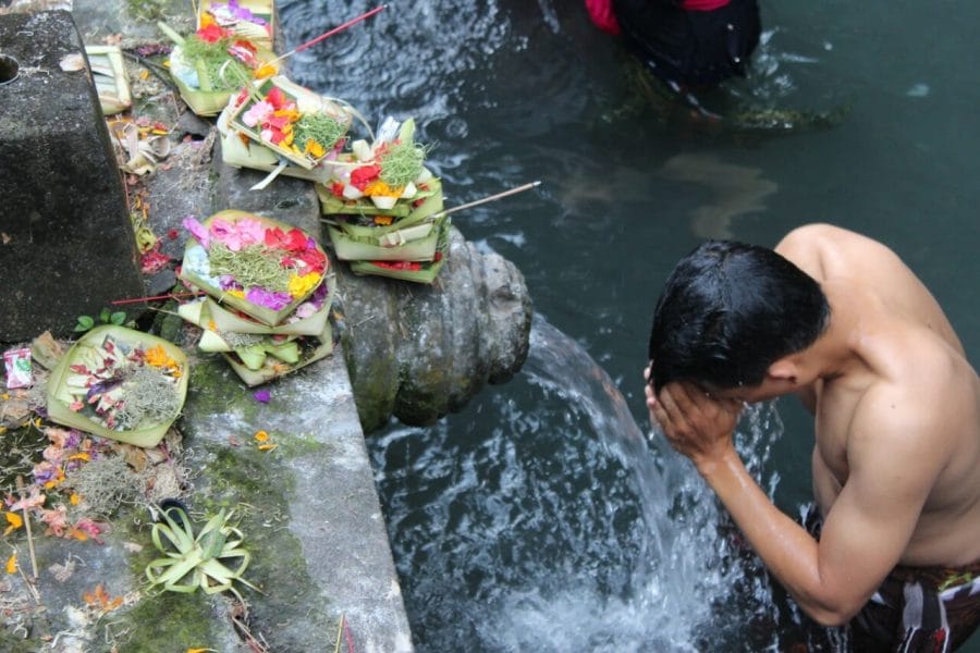 A man half-naked in the water praying near some offers at Tirta Empul, Bali