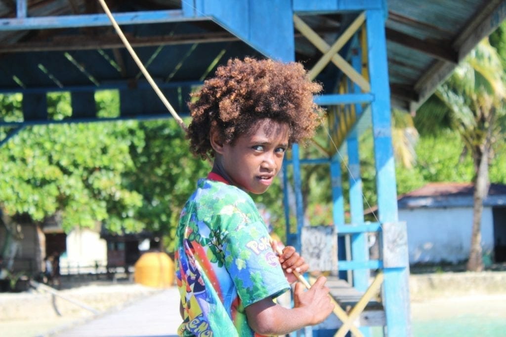 A kid wearing a colourful T-shirt holding a fishing rod in Raja Ampat, Indonesia
