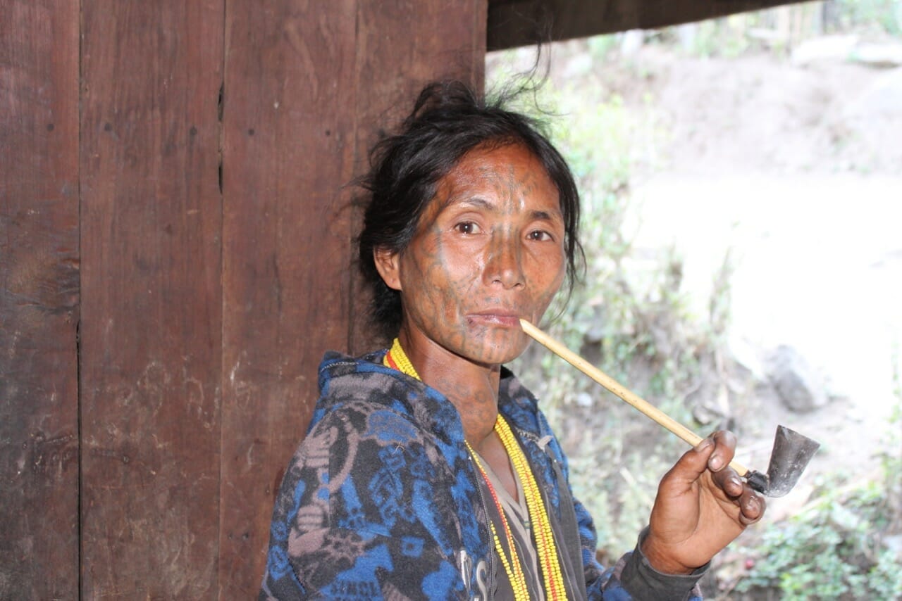 Uma das poucas mulheres com rosto tatuado em Myanmar fumando tabaco num cachimbo de bambu.