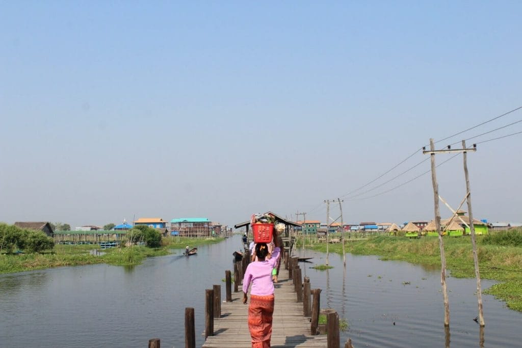 Mulheres andando carregando vasilhas na cabeça em uma ponte que liga o Lago Inle a um povoado local
