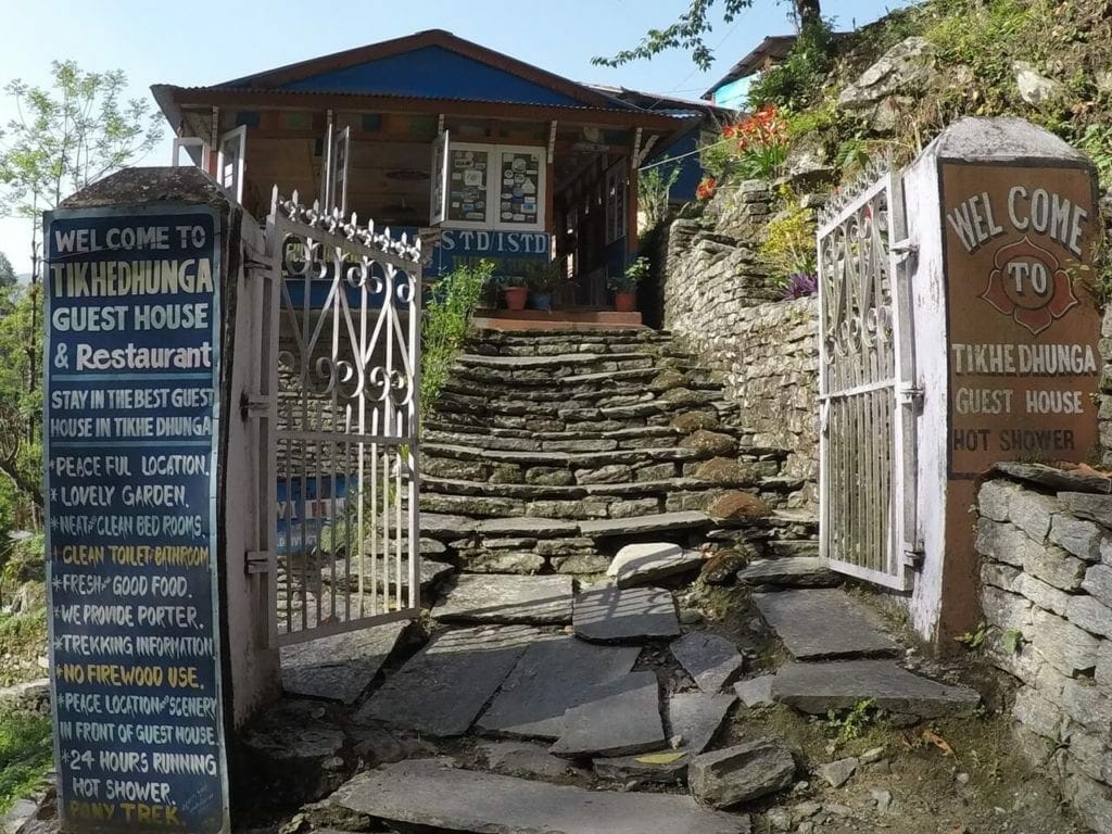 The entrance of Tikhedhunga Guest House, in Nepal, with a white gate, some steps and the reception in the background