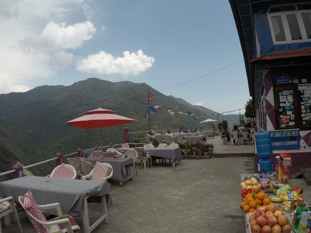 Place Hille Restaurant in Ulleri, Nepal, with some tables, chairs, a counter displaying some fruits and mountains in the background