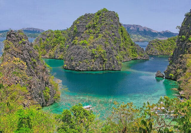 Jagged mountains covered with vegetation and surrounded by crystal-clear turquoise water in Coron, the Philippines.