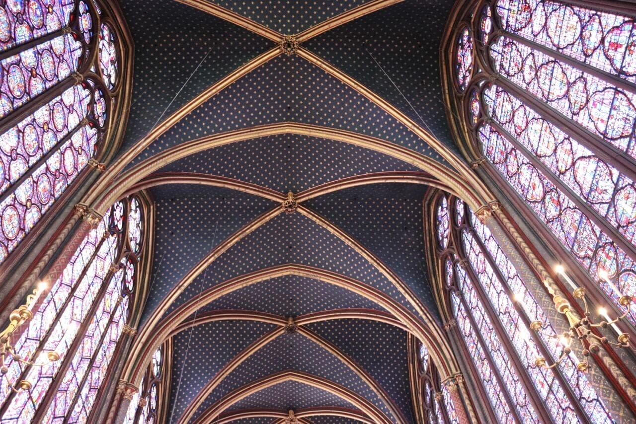 Teto da Saint-Chapelle de Paris com arcos góticos com detalhes dourados e vitrais de vidro de cor vermelho-roxo