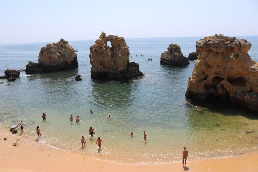 Some people in the water at Praia dos Arrifes, Albufeira, a small beach with three massive isolated rock formations emerging from the water