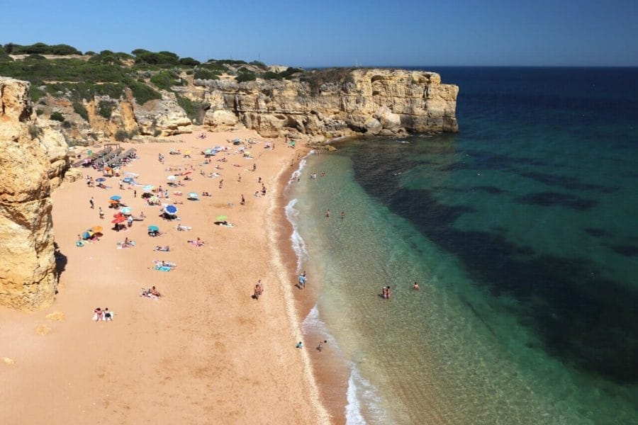 The extraordinary scenery of Praia da Coelha, which's surrounded by yellow limestone cliffs, has soft amber sand and translucent blue water with people sunbathing, walking on the beach and in the water