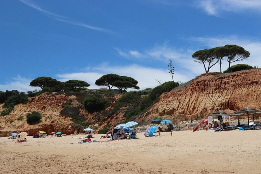 The section of Praia de Santa Eulália, Albufeira, Portugal, bordered by red cliffs topped with trees and low vegetation