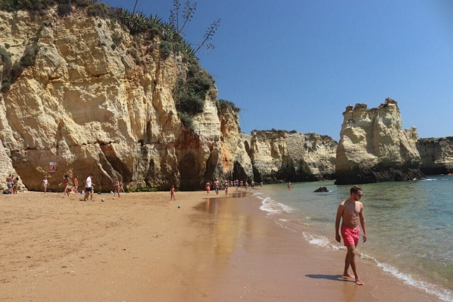 Playas de Lagos, Portugal: 7 Imperdibles + 1 Secreta 14 los enormes acantilados amarillos de Praia do Pinhão, en Lagos, y un hombre con pantalones cortos rosa caminando por la playa