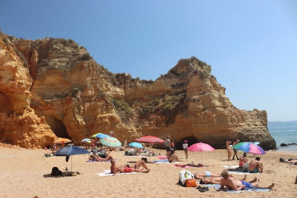 Part of Praia do Pinhão, with some umbrellas, people sunbathing and some yellow cliffs