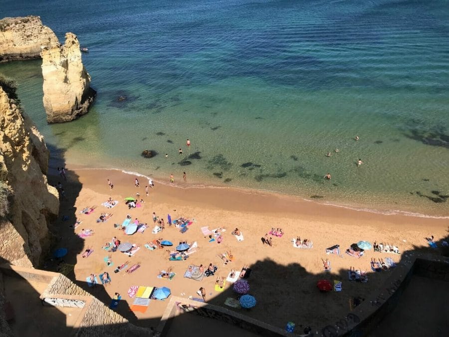 Vista aérea de Praia do Pinhão con mucha gente tomando el sol, otros nadando en las cristalinas aguas azul verdosas y algunos acantilados amarillos