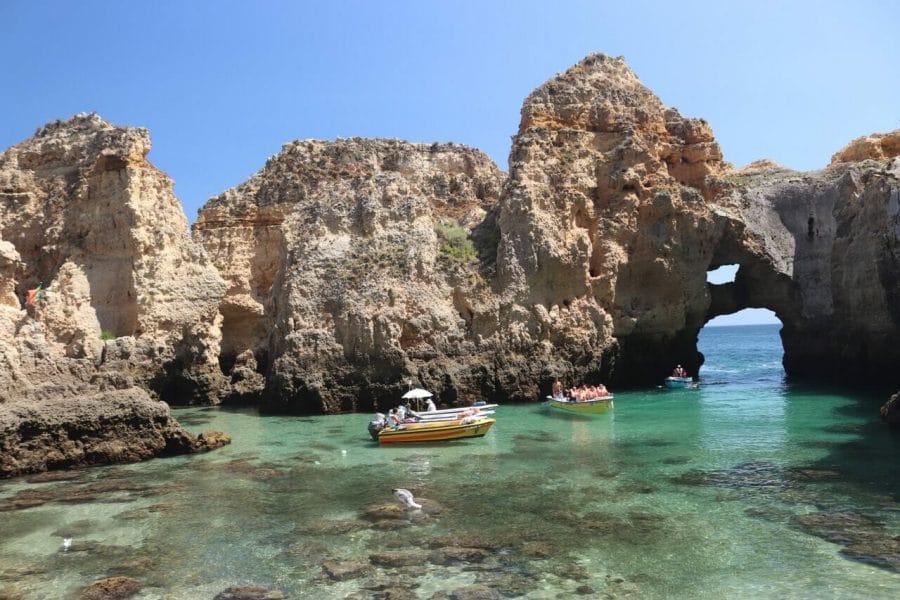 Five boats sailing in the crystalline greet water of Ponta da Piedade, Lagos, Portugal, and ochre limestone cliffs in the background.