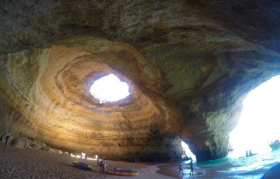 The stunning Benagil Cave in the Algarve, Portugal, and its golden-coloured walls with a round hole in the ceiling and two beautiful archways