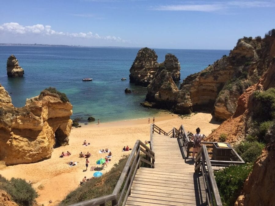 A wooden stairway giving access to Praia do Camilo, Lagos, that's surrounded by red-yellowish cliffs and has calm blue water