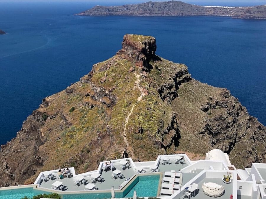 30 Amazing Things to Do in Santorini, Greece 5 A swimming pool and a balcony with tables of a hotel in Imerovigli, Santorini, with the Skaros Rock and the Aegean Sea in the background