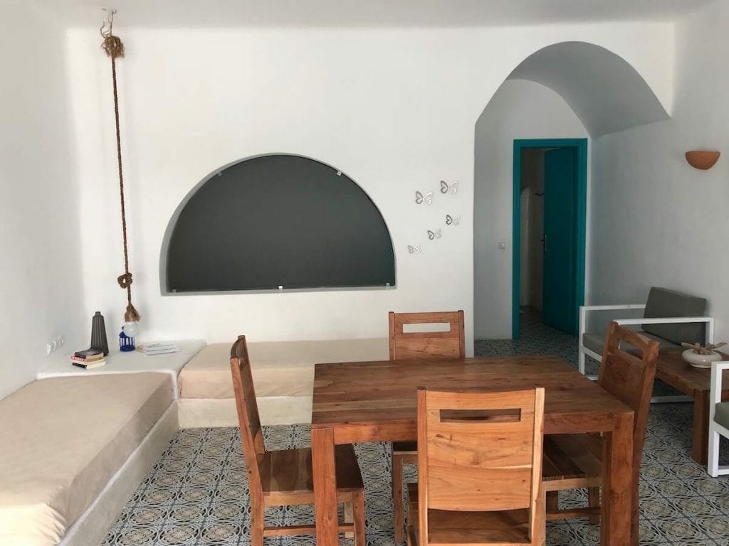 An apartment of Nissia Beach Apartments & Suites in Kamari, Santorini, with white walls, beige sofas and a wooden table with chairs 