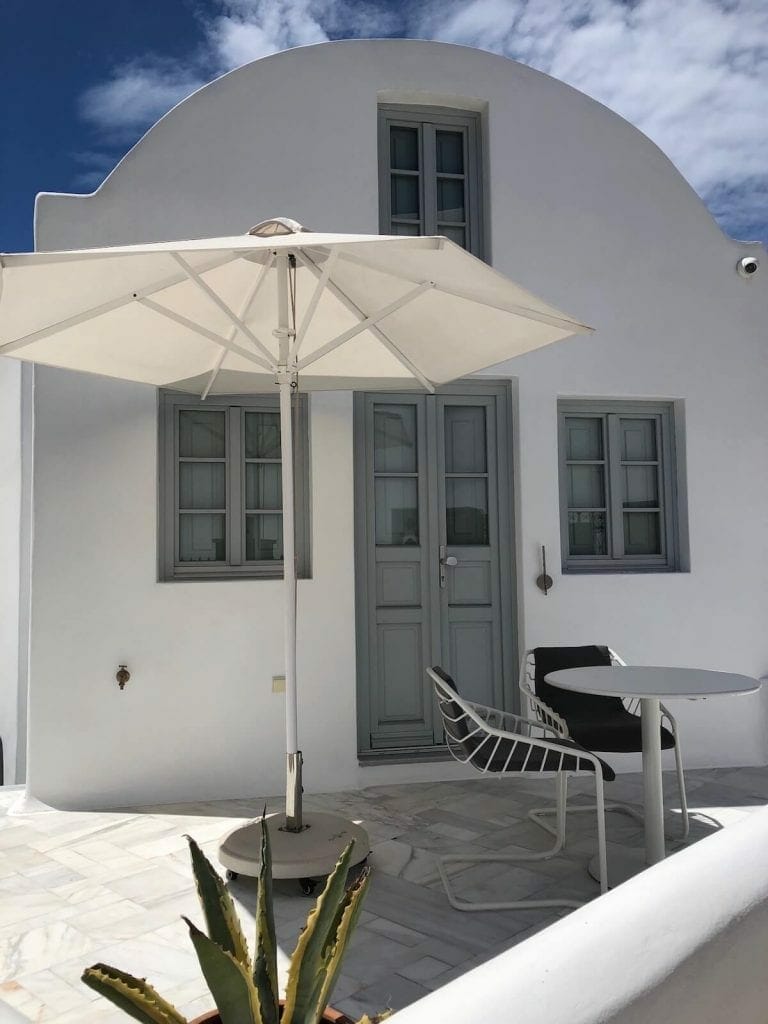 A whitewashed villa with an umbrella, table and chairs on its terrace in imerovigli, Santorini