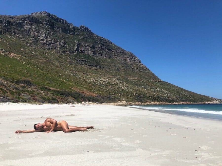Um homem deitado na areia se bronzeando sem roupa em Sandy Bay Beach, na Cidade do Cabo, África do Sul