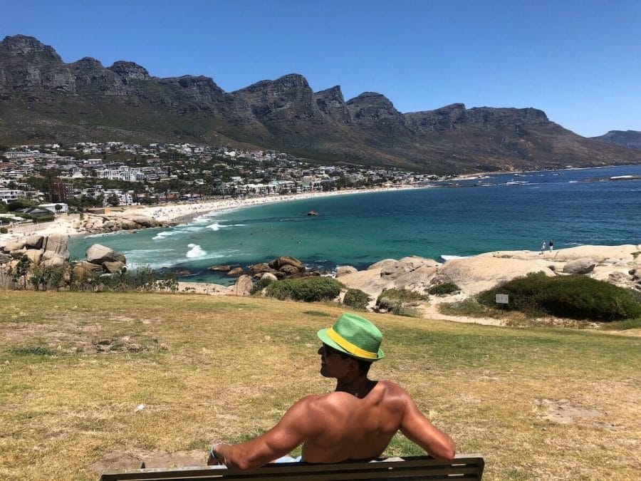 Pericles Rosa seating on a beach admiring the view of Camps Bay, in Cape Town, South Africa