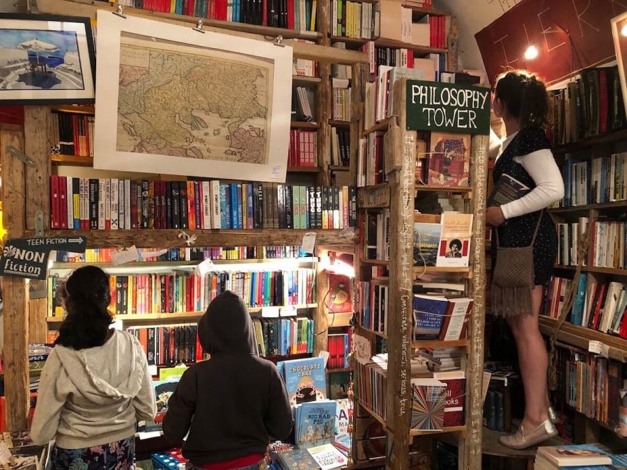 30 Amazing Things to Do in Santorini, Greece 36 Three people among books on the shelves at Atlantis Bookshop, Oia, Santorini