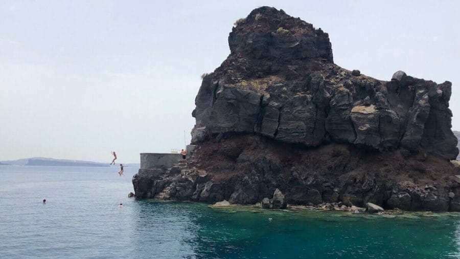 Two ladies cliff jumping from a boulder at Ammoudi Bay, Santorini