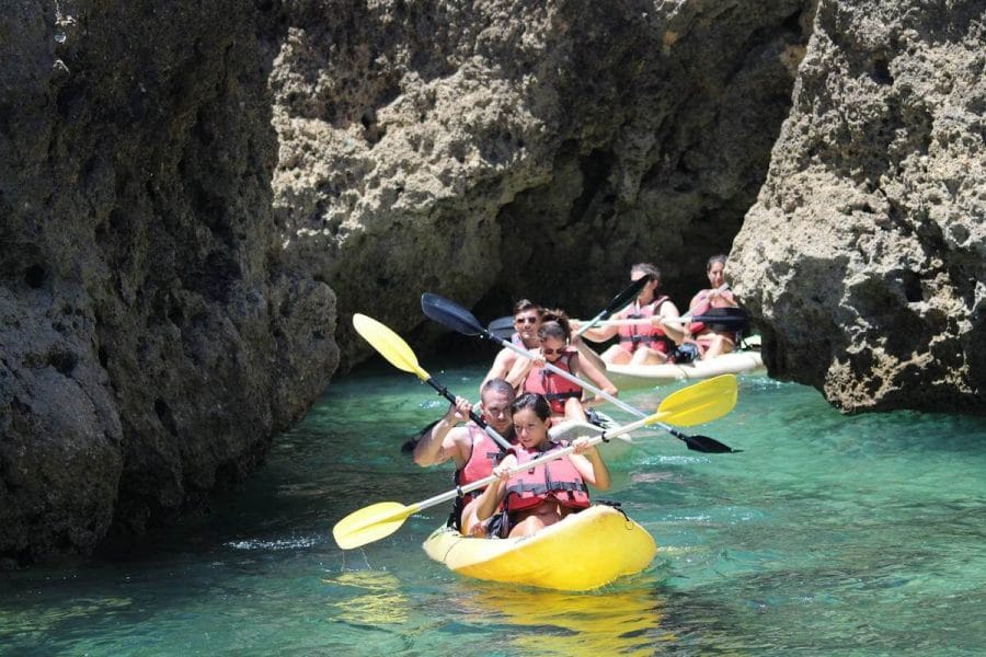 People wearing red lifejackets on yellow kayaks sailing inside a grotto during a tour in Lagos, Algarve