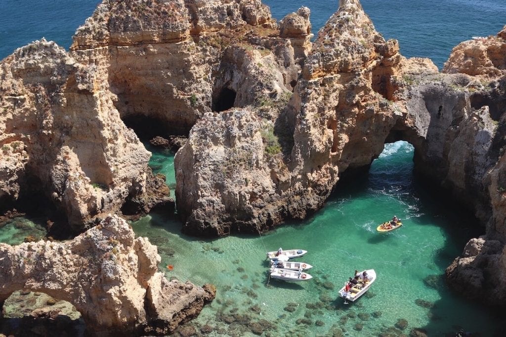 Four boats sailing in the crystalline waters of Ponta da Piedade, Lagos, that's surrounded by massive ochre limestone cliffs and extraordinary rock fformations