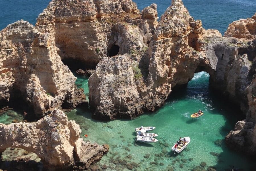Five boats sailing in the crystalline green water of Ponta da Piedade, Lagos, surrounded by colossal ochre limestone cliffs and incredible formations