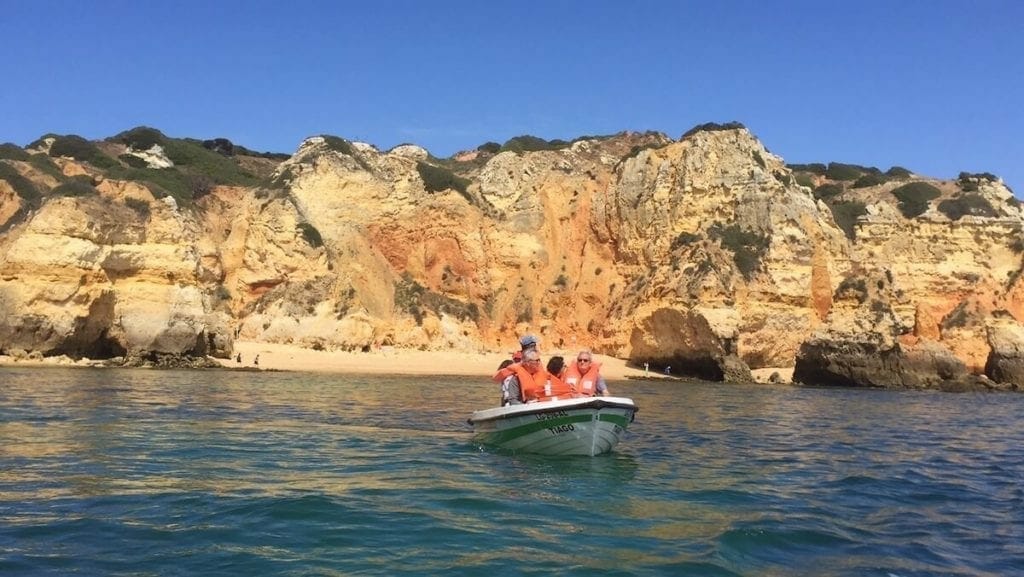 three people wearing red lifejackets on a boat trip to Ponta da Piedade and massive yellow limestone cliffs in the background