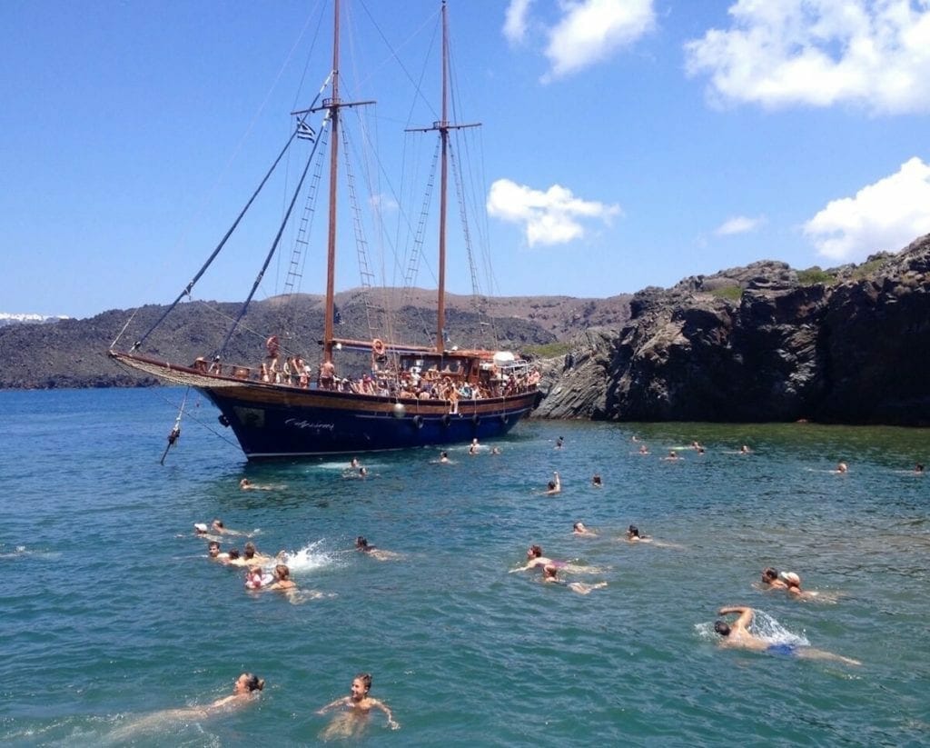people swimming on a hot spring in Santorini and others on a boat during a caldera tour