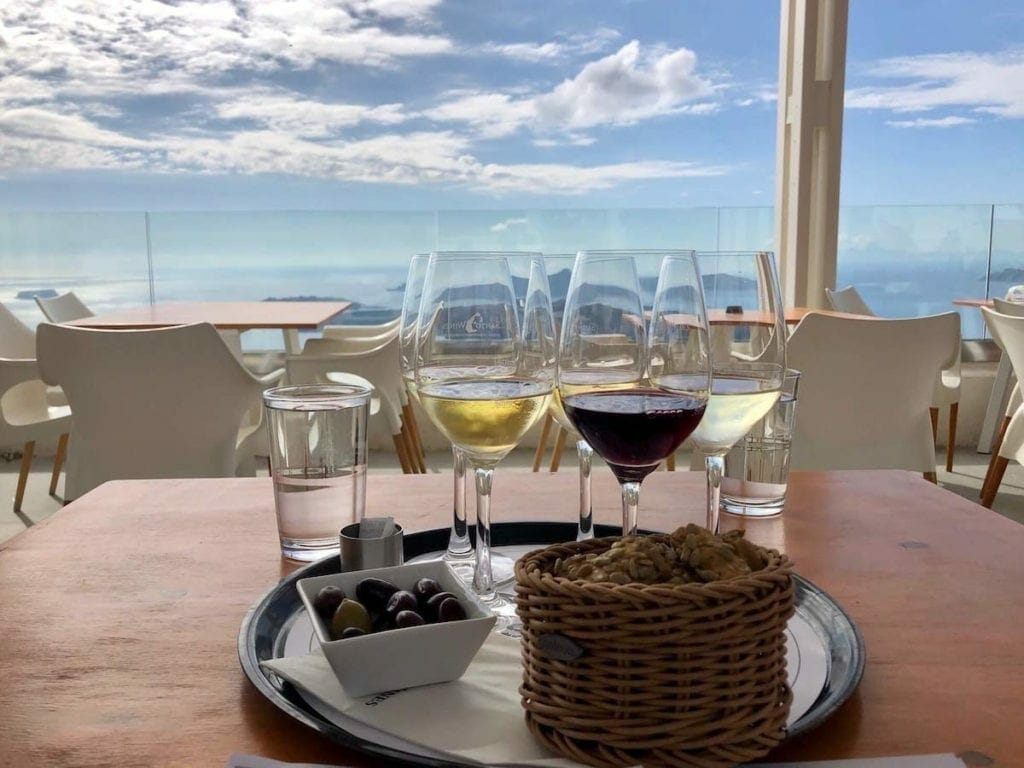 a trail with four glasses with some red and white wine, a basket with some bread and a white bowl with olives served during a wine tasting at Santo Wines, Santorini