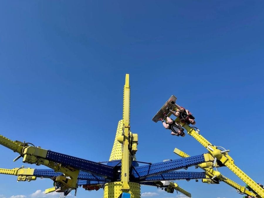 Duas pessoas sentadas, de cabeça para baixo, no brinquedo Air Race, do parque de diversões que fica no Brighton Palace Pier, na cidade de Brighton, Inglaterra