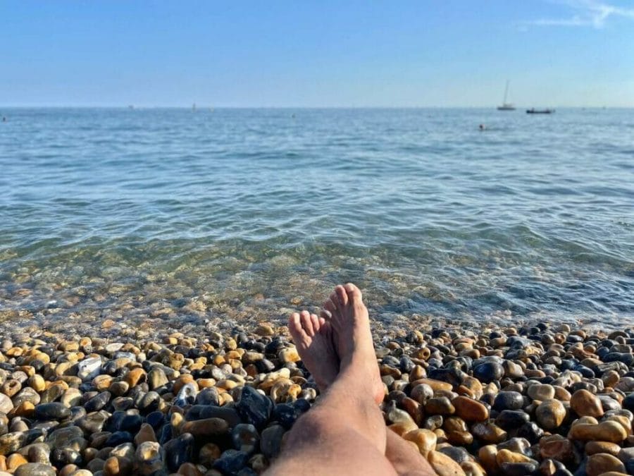 Um par de pernas cruzadas deitadas nas pedras em frente ao mar em Brighton Beach, Inglaterra