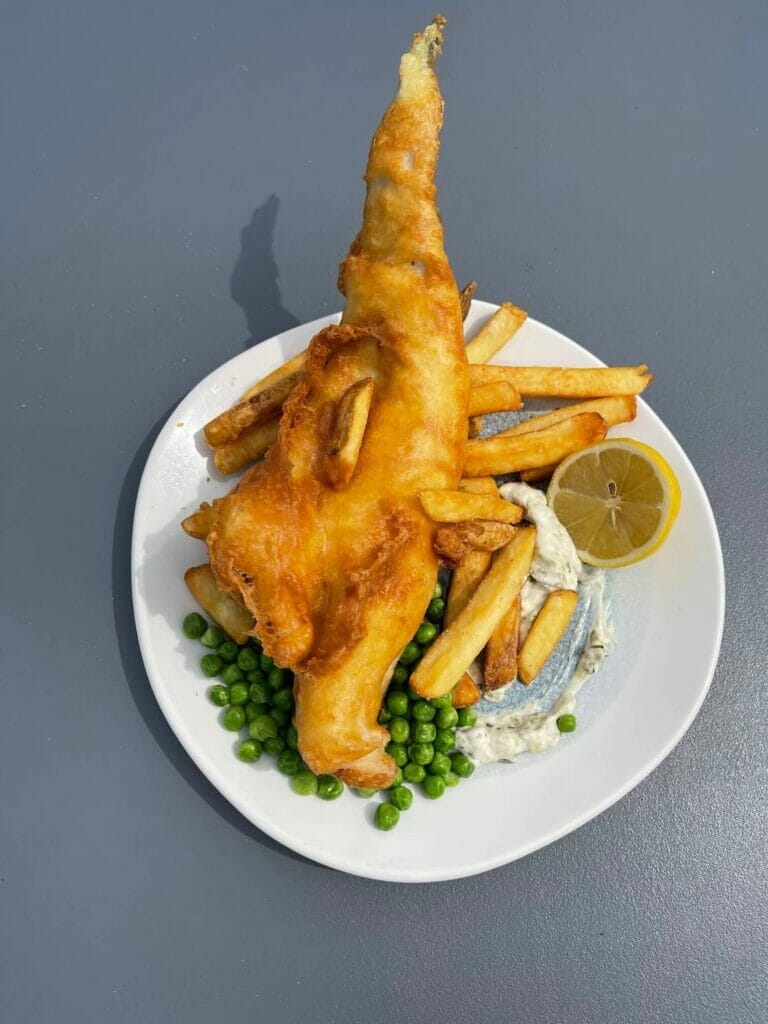 Um prato branco com peixe e batatas fritas servidos no Brighton Beach Club