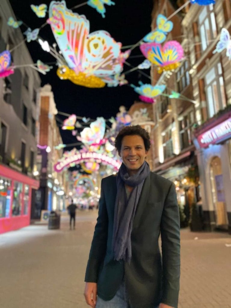 Melhores Luzes de Natal em Londres 2021 - Lugares Imperdíveis 5 Péricles Rosa usando um blazer verde e cachecol azul curtindo carnaby Street Luzes de Natal