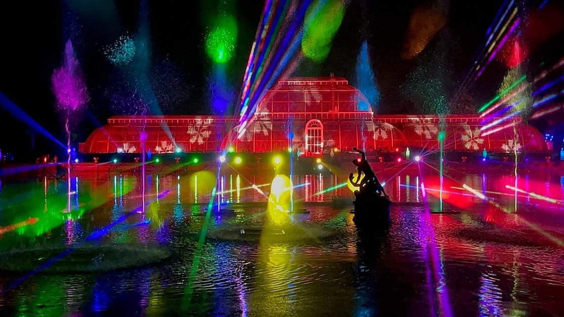 A stunning lighting projection across the historic glasshouse and adjacent lake during Kew Gardens Christmas Lights