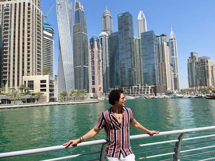 Péricles Rosa posando para uma foto no Dubai Marina Walk com alguns arranha-céus enormes como pano de fundo
