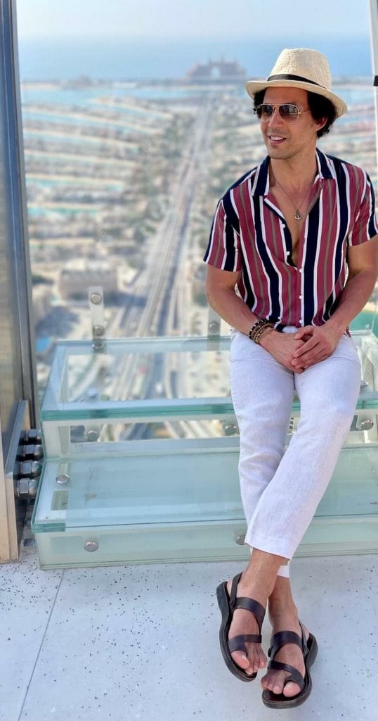 Pericles Rosa con sandalias, pantalones de línea beige, camisa a rayas, gafas de sol y un sombrero en The View at The Palm, Dubai