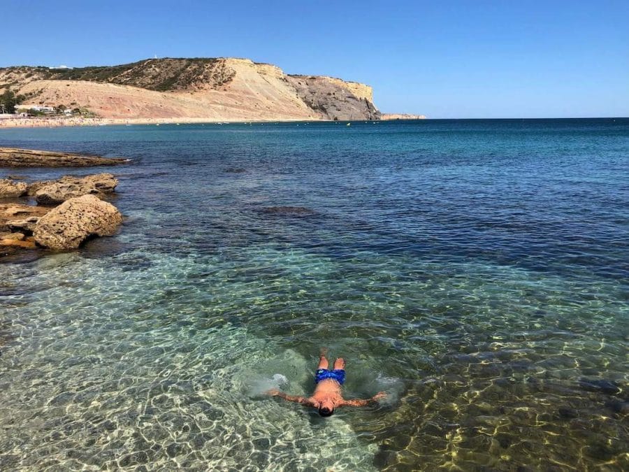 18 Best Things to Do in Lagos, Portugal 16 A man swimming in the crystal-clear water of Praia da Luz, Lagos, Portugal