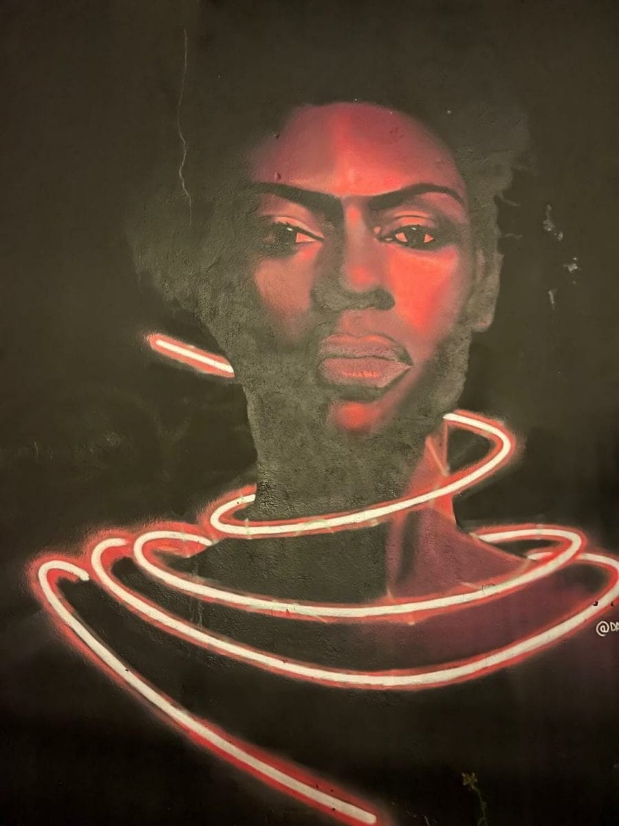 A neon pink face portrait mural of a woman by David Speed on Braithwaite St, London
